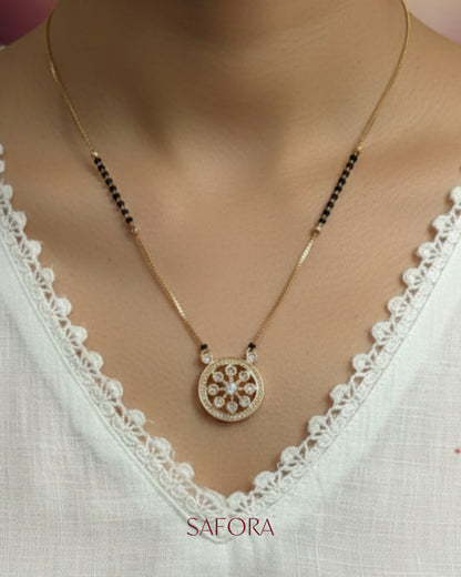 Gold necklace with a decorative pendant on a white lace top, branded 'Safara'.