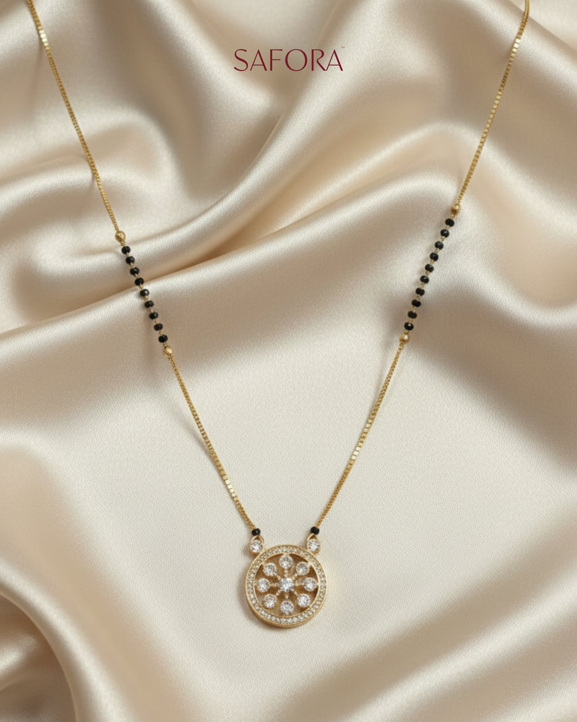 Gold necklace with a pendant on a beige fabric background, featuring the brand 'SAFORA'.