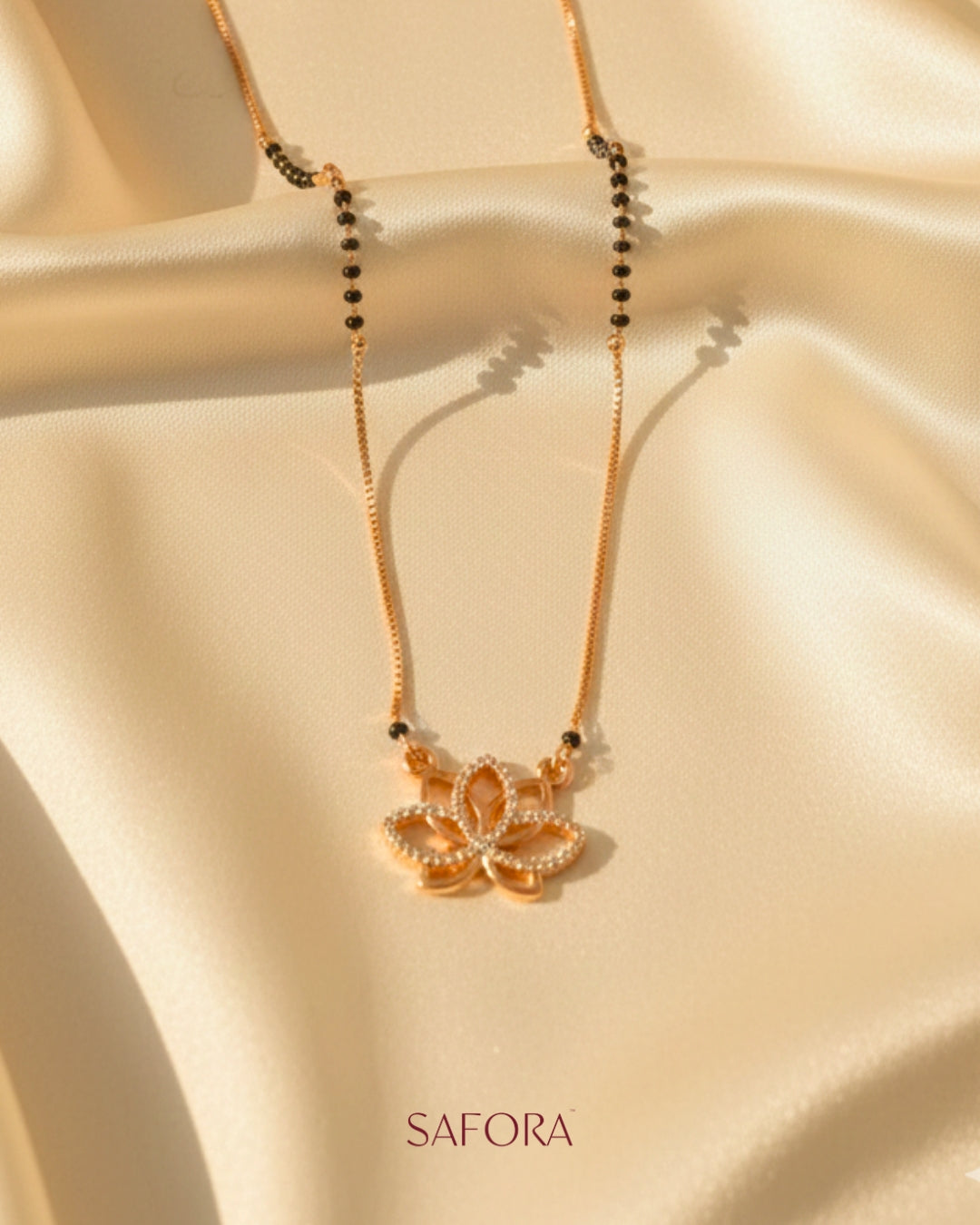 Gold necklace with a pendant on a beige fabric background, featuring the brand 'SAFORA'.
