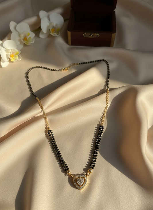 Necklace with black beads and a heart-shaped pendant on a beige fabric background with white flowers and a wooden box.