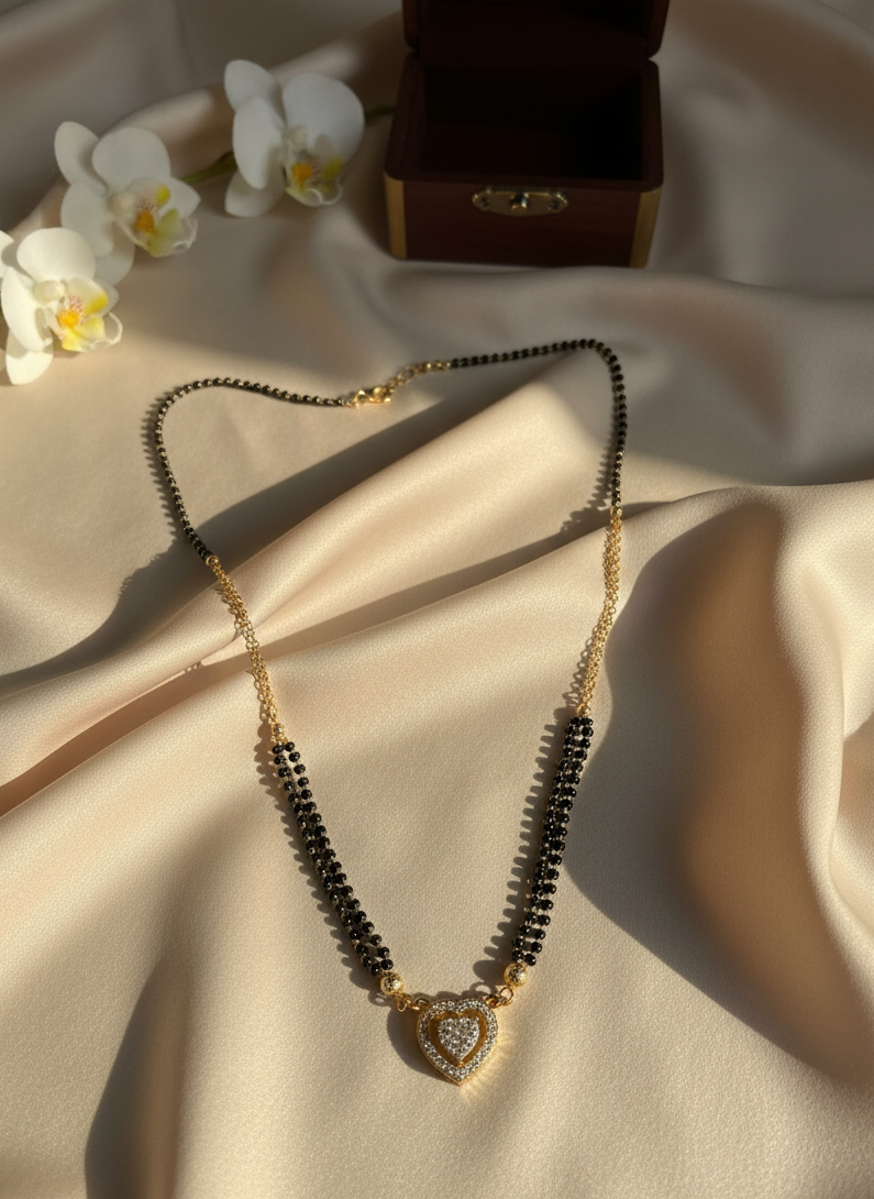 Necklace with black beads and a heart-shaped pendant on a beige fabric background with white flowers and a wooden box.