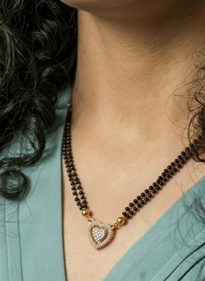 Close-up of a person wearing a black beaded necklace with a heart-shaped pendant, branded 'SAFORA'.